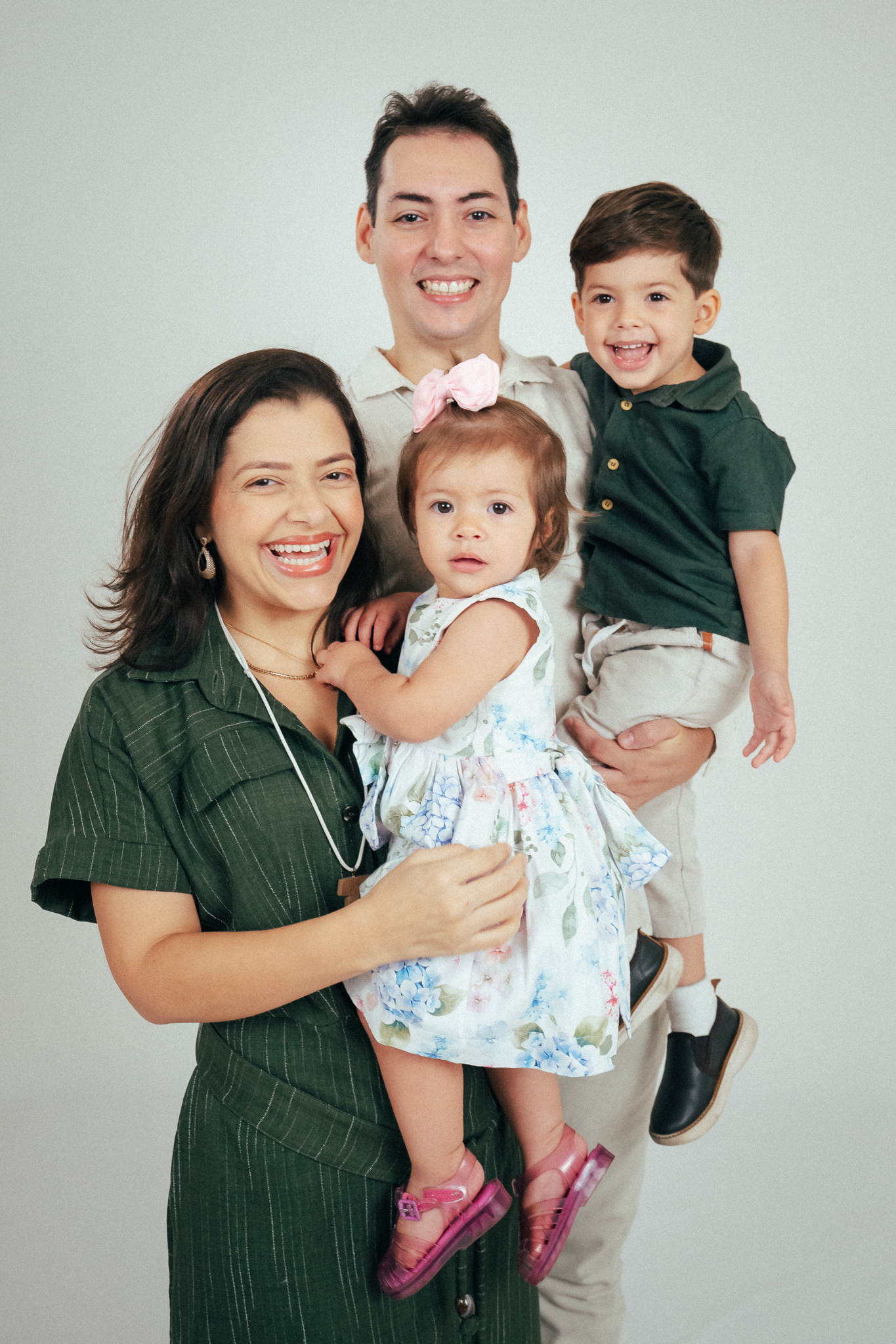 Foto em estúdio de uma família sorridente: homem e mulher segurando um menino e uma menina de colo.