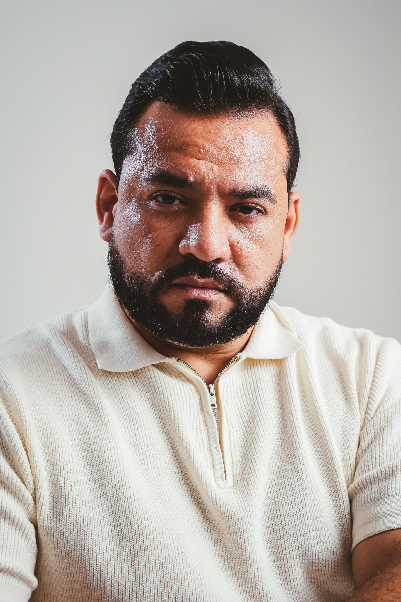 Retrato corporativo em plano médio de homem de cabelo escuro penteado para trás e barba, usando camisa polo clara contra fundo neutro.